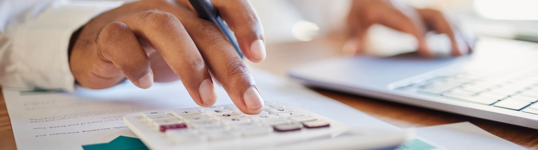 a man's hand working on a budget with a calculator and laptop