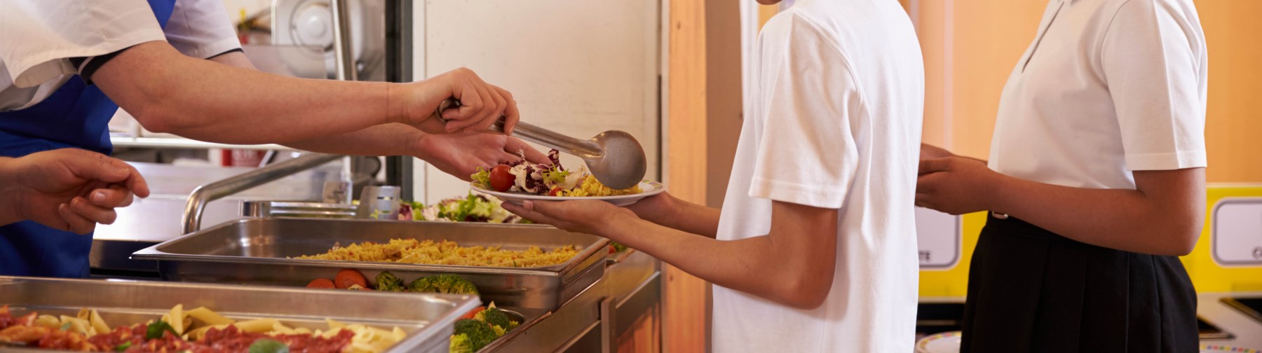 male student with a lunch tray being served food in the school cafeteria