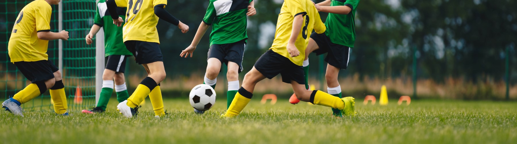 feet of children in green and yellow uniforms playing soccer